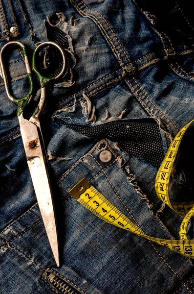 Tailoring and design concept. Scissors, measuring tape and ripped jeans. Old metal scissors and a yellow tailor meter. Tailor services. Close-up. Copy space.