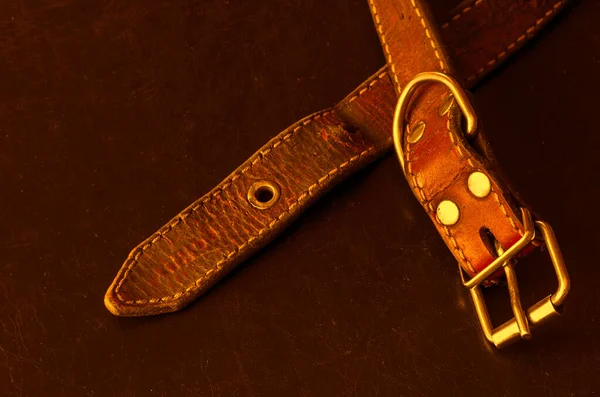 Old red leather dog collar. A close-up of a shabby and cracked dirty collar on a dark table. Love to the animals. Vintage Collectibles. Selective focus.