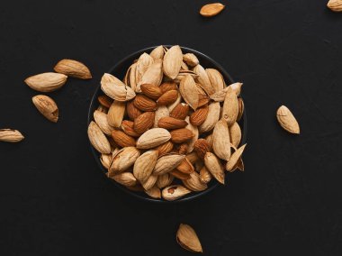 Siyah arka plandaki doğal organik bademler. Kasenin etrafına fındıklar saçılmış. Düz yatıyordu. Sağlıklı beslenme konsepti. Doğal ışık.