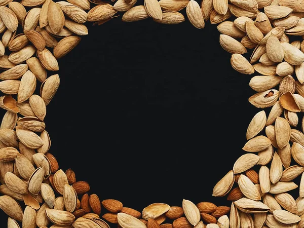 Natural organic almonds are laid out in a circle on a black background. Top view, copy space in the center. Healthy eating concept. Natural light.