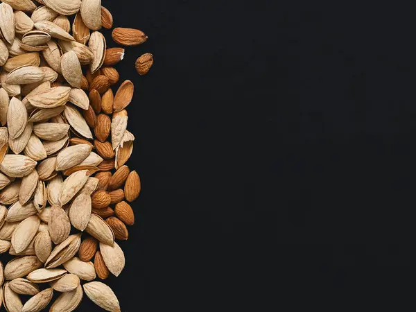 Natural organic almonds on the left side of a black background. Top view, copy space. Healthy eating concept. Natural light.