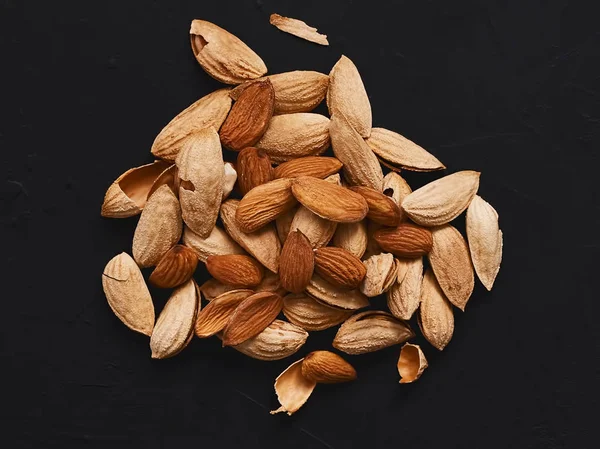 Natural organic almonds are laid out in a pile in the center on a black background. Top view. Healthy eating concept. Natural light.