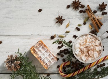 Beyaz ahşap bir masada sıcak kakao ve lokum. Baharatların arka planında sıcak içecekler için kakule, anason, tarçın. Yakınlarda kozalaklı dallar ve taze waffle 'lar var. Üst görünüm.