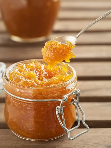Tasty, homemade orange jam in a glass jar on a vintage wooden background. Dessert spoon with jam over the jar. Healthy citrus dessert. Close-up — Stock Photo, Image