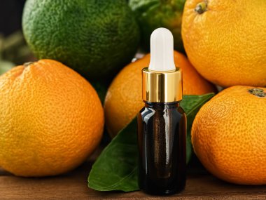 Mandalinalarla çevrili ahşap bir arka planda cam bir şişenin içindeki mandalina yağı (citrus). Yakın plan. Seçici odak.