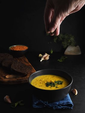 Kırmızı mercimek çorbası, baharatlar, otlar, sebzeler ve krema. Mavi peçeteli çorba, kahverengi ekmek, sarımsak, mercimekli bir kase. Kadın eli çorbaya baharat ekler. Yakın plan..