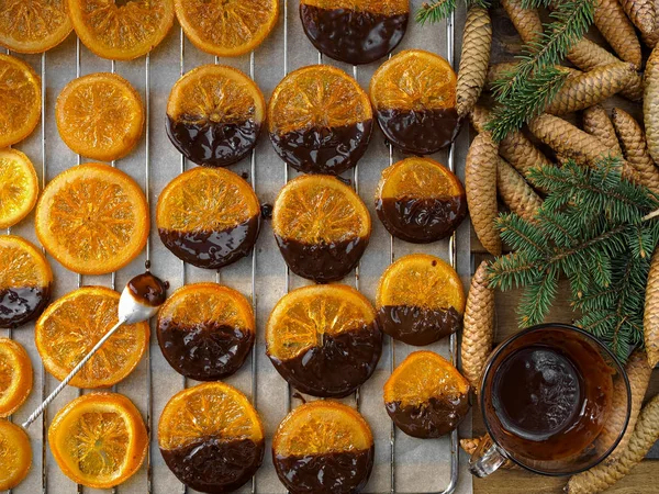 Christmas sweets, candied fruits in chocolate. Caramelized orange slices on a light paper background. Homemade dessert. Slices laid out on paper, top view. Decor - branches and cones of spruce. — Stock Photo, Image