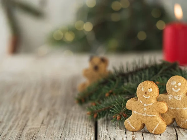 Noel ev yapımı zencefilli kurabiye, zencefilli kurabiye adam. Çam ağacının dalları ve yanan bir mumun yanında, eski bir ahşap arka planda. Yakın plan..