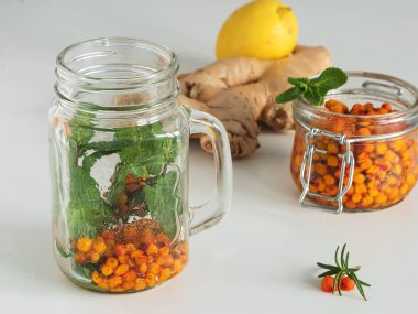 Çay malzemelerinin yanında beyaz bir arka planı olan içecek konteynırı. Kış içkileri. Naneli, zencefilli, limonlu, deniz dikenli ve ballı çay. Yakın plan..