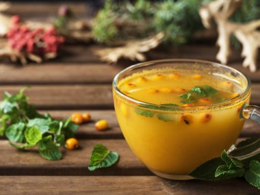 Deniz dikenli ve zencefilli faydalı bitki çayı. Nane yaprakları ve deniz dikenli cam bardak sıcak çayla doludur. Yakın plan. Ahşap arka planda sonbahar yaprakları.