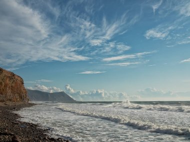 Sonbahar ve kış deniz fırtınası, güneşli bir gün. Kaya sahili, taş plajı. Bulutlu mavi gökyüzü. Karadeniz 'in kuzey kıyısı.