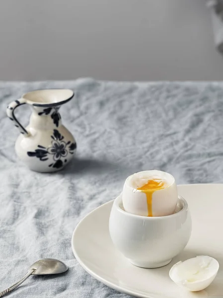 Soft-boiled egg, light breakfast. White ceramic plate with soft-boiled egg, on a white ceramic plate, on a blue tablecloth. Vintage gravy boat. Morning, healthy continental breakfast. Close-up.