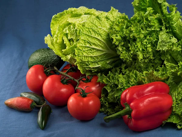 緑のサラダ、中国のキャベツ、ハラペーニョ、アボカド、野菜、青の織物の背景に新鮮なトマト。接近中だレタスの葉に焦点を当てます。水平方向. — ストック写真