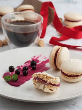 Gri bir tabakta üzümlü ev yapımı badem kurabiyesi. Frenk üzümü, nane yaprakları ve bir tabakta bisküvi. Yakın plan. Hediye paketi için kırmızı kurdele ve arka planda bir fincan kahve..