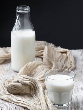 Sütlü cam, ahşap bir mahsulün yüzeyine yakın plan. Arka planda bir şişe süt var. Doğal süt ürünleri. Dikey oryantasyon. Sığ alan derinliği.