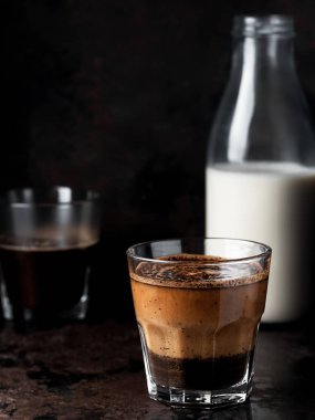 İki bardak sütlü kahve, soğutucu bir içecek buzlu kahveydir. Cam koyu metal bir arka planda bulunuyor. Yakın çekim, dikey yönelim, metin için boşluk. Sığ alan derinliği.