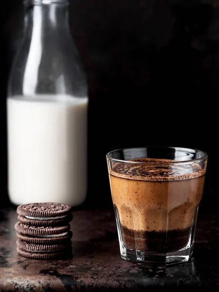 A glass of coffee with milk, a cooling drink is ice coffee. The glass is located on a dark metal background. Near chocolate cookies. Close-up, space for text. Shallow depth of field.