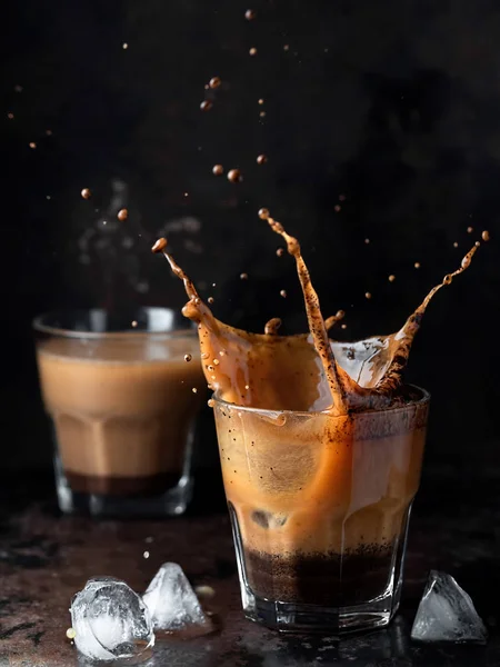Koyu arka planda buzlu kahvenin olduğu bardağa su sıçrat. Buzlu cappuccino içeceğini buz küpleriyle tazeliyorum. Soğuk bir içecek dalgası. Yakın çekim, dikey yönelim, metin için boşluk. Sığ alan derinliği.