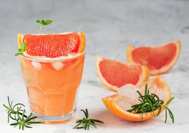 Soğuk limonata taze greyfurt suyu, alkol ve buz küpleri gri arka planda bir dilim greyfurt, dal nane ve biberiye süsledi. Uzayı kopyala Yaklaş, seçici odaklanma.