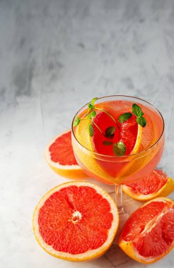 Alkol ve buz küplü soğuk greyfurt suyu, gri arka planda bir dilim greyfurt ve nane şekeri ile süslenmiş. Uzayı kopyala Yaklaş, seçici odaklanma. Greyfurt dilimlerinin yanında..