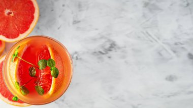 Alkol ve buz küplü soğuk greyfurt suyu, gri arka planda bir dilim greyfurt ve nane şekeri ile süslenmiş. Uzayı kopyala Üst görünüm, seçici odaklanma. Greyfurt dilimlerinin yanında..