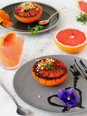 Mor, ceviz, biberiye ve balzamik sosla süslenmiş çay tabağında kahverengi şekerli fırında greyfurt. Sonra da bir bardak üzüm suyu. İki kişilik sağlıklı bir vejetaryen kahvaltısı..