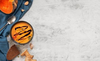 Balkabağı kremalı çorba, balsamil souse ve zeytinyağı. Süslü biberiye kepeği ve kabak çekirdeği. Geleneksel malzemeler, sağlıklı gıda konsepti. Mavi peçete, gri arkaplan, kopyalama alanı, üst görünüm.