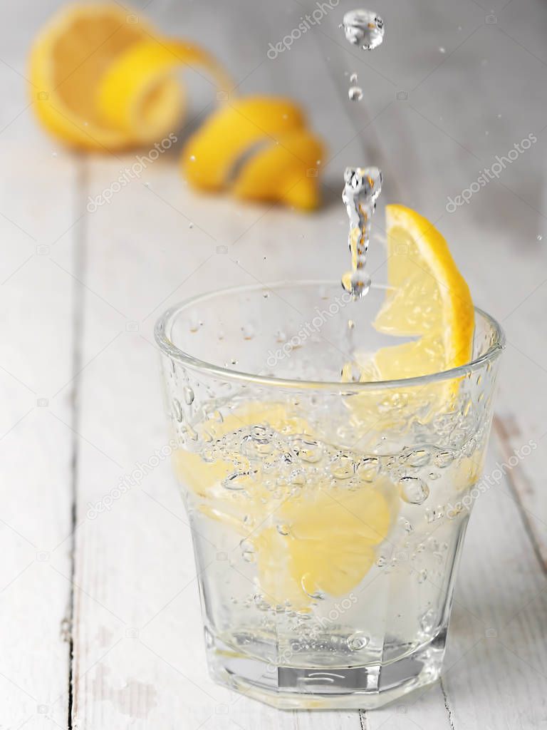 Pouring lemonade into a glass with ice, flow and splash. White wooden vintage background. Close up, shallow depth of field.