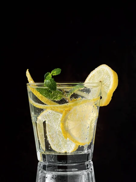 Cold drink on a black background. One glass with lemonade or mojito cocktail with lemon and mint. Copy space, close up. — Stock Photo, Image