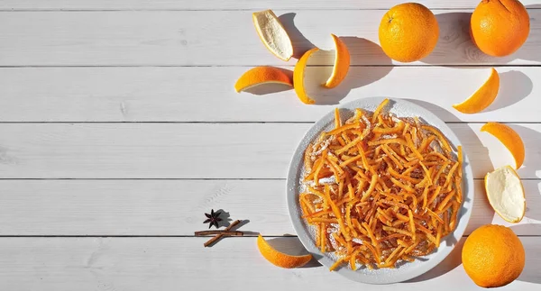 Candied orange peel in sugar is a favorite treat for children and adults. Image of homemade candied oranges peel and orange on the white wooden table. Top view, copy space