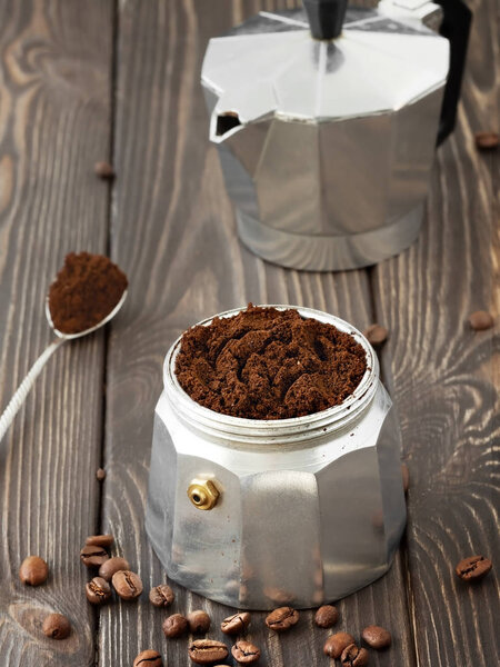 Roasted coffee beans in a glass jar, scattered on a wooden brown table. Hand mill and coffee pot (la moka) in the background. Close-up, soft focus, concept of traditional coffee preparation.