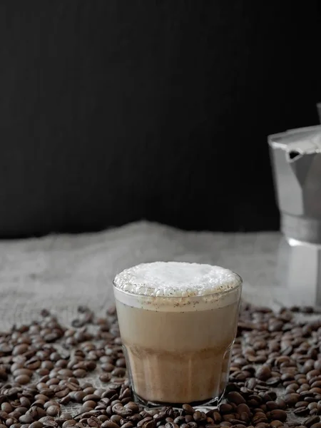 Gelas cangkir kopi dengan susu di latar belakang kayu gelap. Latte panas atau cappuccino disajikan dengan susu di antara biji kopi yang tersebar di burlap. Close-up, soft focus, copy space . — Stok Foto