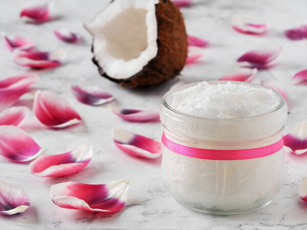 Кокосовое масло и кокосы на деревянном белом фоне. Розовые лепестки цветов на столе. Закрыть
.