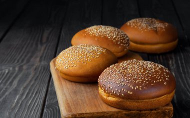Koyu ahşap arka planda susamlı taze pişmiş hamburger çörekleri. Susamlı ya da ekmekli yuvarlak çörek. Yakın çekim.