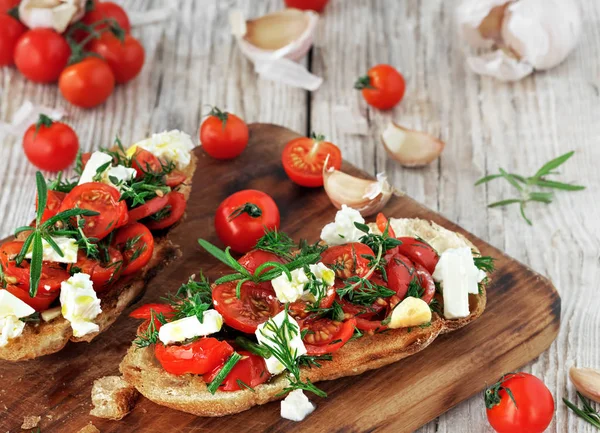 Tost, domatesli tost, feta peyniri ve taze aromatik otlar, biberiye, dereotu, sarımsak eski bir köy masasında. Geleneksel İtalyan aperatifi veya aperatifi, antipasto. Kapat.
