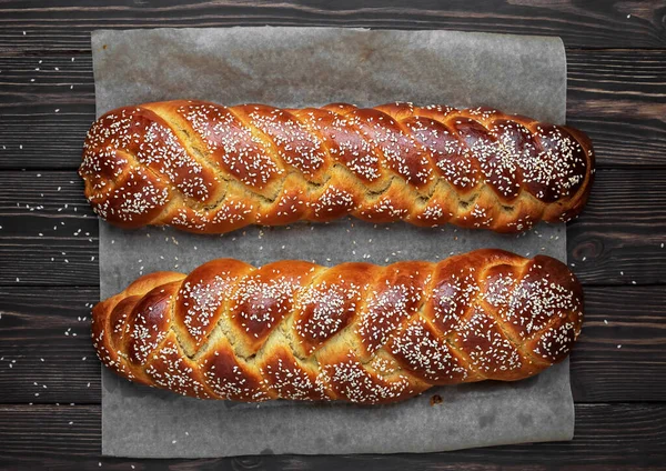 Fırında pişmiş taze tatlı ekmek (challah ekmek) bir kabartma kağıdı üzerinde, koyu ahşap arka plan, üst görünüm.
