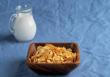 Sütlü sürahi, tahıl gevrekleri ahşap bir tabakta mavi masa örtüleri. Yaklaş. Sığ alan derinliği.