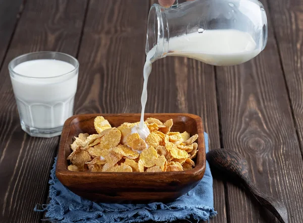 Milk splash on wooden bowl with a cereal corn flakes. Dark wooden backgraund, close up. Shallow depth of field.