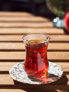 Loggia 'daki ahşap bir masanın üzerinde, çay bardağında çay. Arka planda çiçekler ve olgun nar var. Parlak güneşli bir gün. Yakın plan..