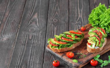 Ciabatta ekmeğinde avokado sandviçi. Taze kesilmiş avokado ve sebzelerle yapılmış. Koyu ahşap bir masada sağlıklı vejetaryen kahvaltısı. Kopyalama alanı ile yakınlaş