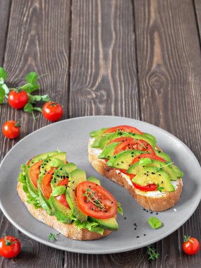 Ciabatta ekmeğinde avokado sandviçi. Yukarıdan taze kesilmiş avokado ve sebzelerle yapılmış. Koyu ahşap bir masada sağlıklı vejetaryen kahvaltısı. Kopyalama alanı ile yakınlaş