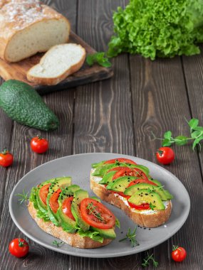 İki ciabatta tostu, doğranmış avokado, domates, zeytinyağı, peynir, marul ve siyah susam tohumu. Sağlıklı vejetaryen kahvaltısı..