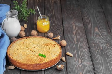 Ev yapımı İsviçre Kapalı Cevizli Turta ve badem ve ceviz. Bir sürahi süt, portakal reçeli ve fındık yanında, koyu ahşap bir masanın üzerinde. Tatil pastası. Yakın plan, metin için boşluk kopyala.