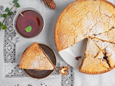 Ev yapımı İsviçre usulü, badem ve cevizli kapalı cevizli turta. Dilimlenmiş turta, dantelli beyaz bir masa örtüsünün üzerinde. Yakınlarda bir fincan kırmızı çay var. Tatil ziyafeti. Üst görünüm.