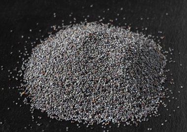 Siyah taştan bir arka planda haşhaş tohumu yığını, yakın plan. Ekmek ve tatlı pişirmek için gerekli malzemeler.