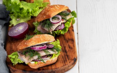 İskandinav mutfağı, deniz ürünleri burger, taze kızarmış çörek, ringa filetosu, soğan ve marul. Tabak, ahşap bir tahtanın üzerinde servis edildi. Yakın çekim, alan derinliği.