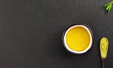 Siyah taştan bir arka planda kibrit yeşil çay bardağı. Çay yaprakları ve yanında çay olan tahta bir kaşık. Üst manzara, çay seremonisi, minimalizm, kopyalama alanı.