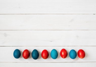 Beyaz ahşap zemin üzerine boyanmış Paskalya yumurtaları, üst görünüm, metin için kopyalama alanı.