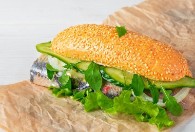 Herring fileto sandviçi, soğanlı Haringhandel, salatalık ve kağıt üzerinde salata. Metin için kopyalama alanı olan beyaz ahşap bir arkaplan. İskandinav mutfağında geleneksel sokak yemekleri.