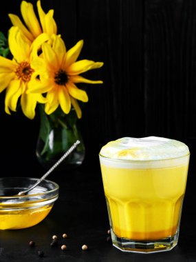 Siyah arka planda zerdeçal, bal ve diğer baharatlı altın süt. Grip ve soğuk algınlığından korunmak için geleneksel içecek. Yakın plan, baharatlar ve içecekler masada..